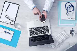 Doctor working at office desk, using a telehealth software enabled mobile