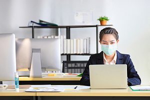 Employee wearing mask working alone. Teleworking present certain cybersecurity risks to employers and employees