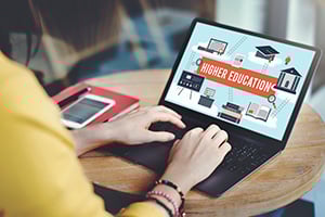 Person sitting at laptop with the words higher education on the screen.