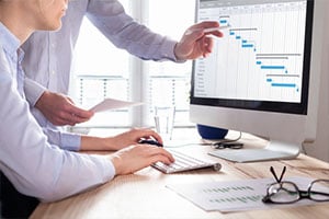 Project management team updating Gantt chart schedule or planning on computer, two business people in office