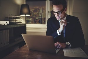 serious businessman working on laptop at night sitting in office looking concentrated