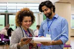 two educators reviewing their plans on a notebook in the hallway